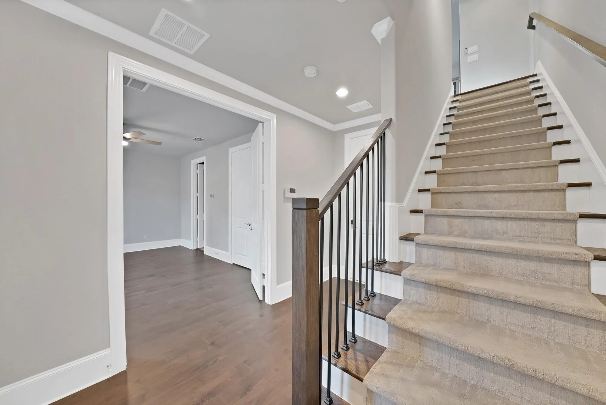 Staircase with carpeted treads, wood risers, and a wrought iron baluster