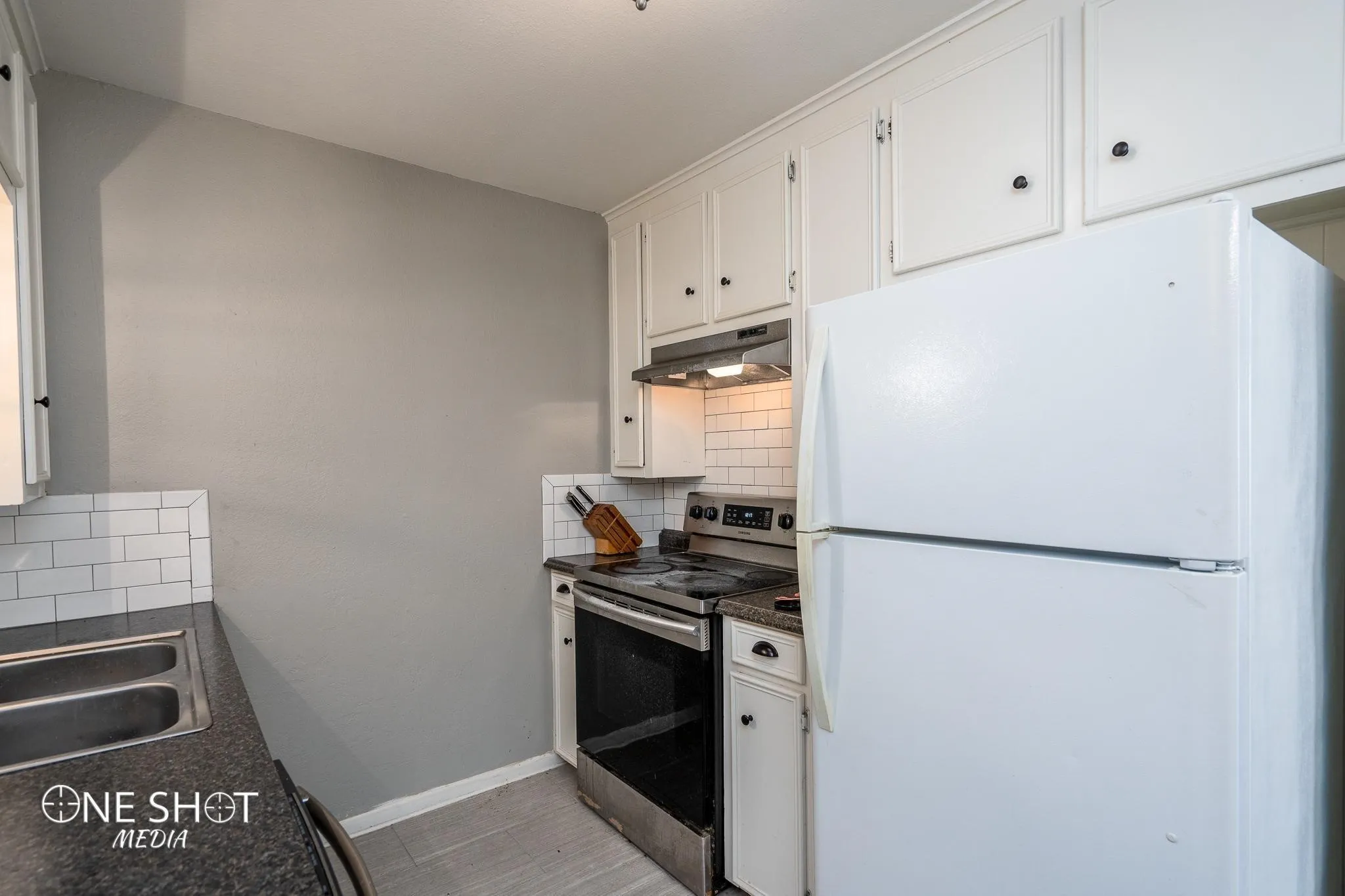 Kitchen with stainless steel range with electric stovetop, backsplash, white refrigerator, sink, and white cabinetry