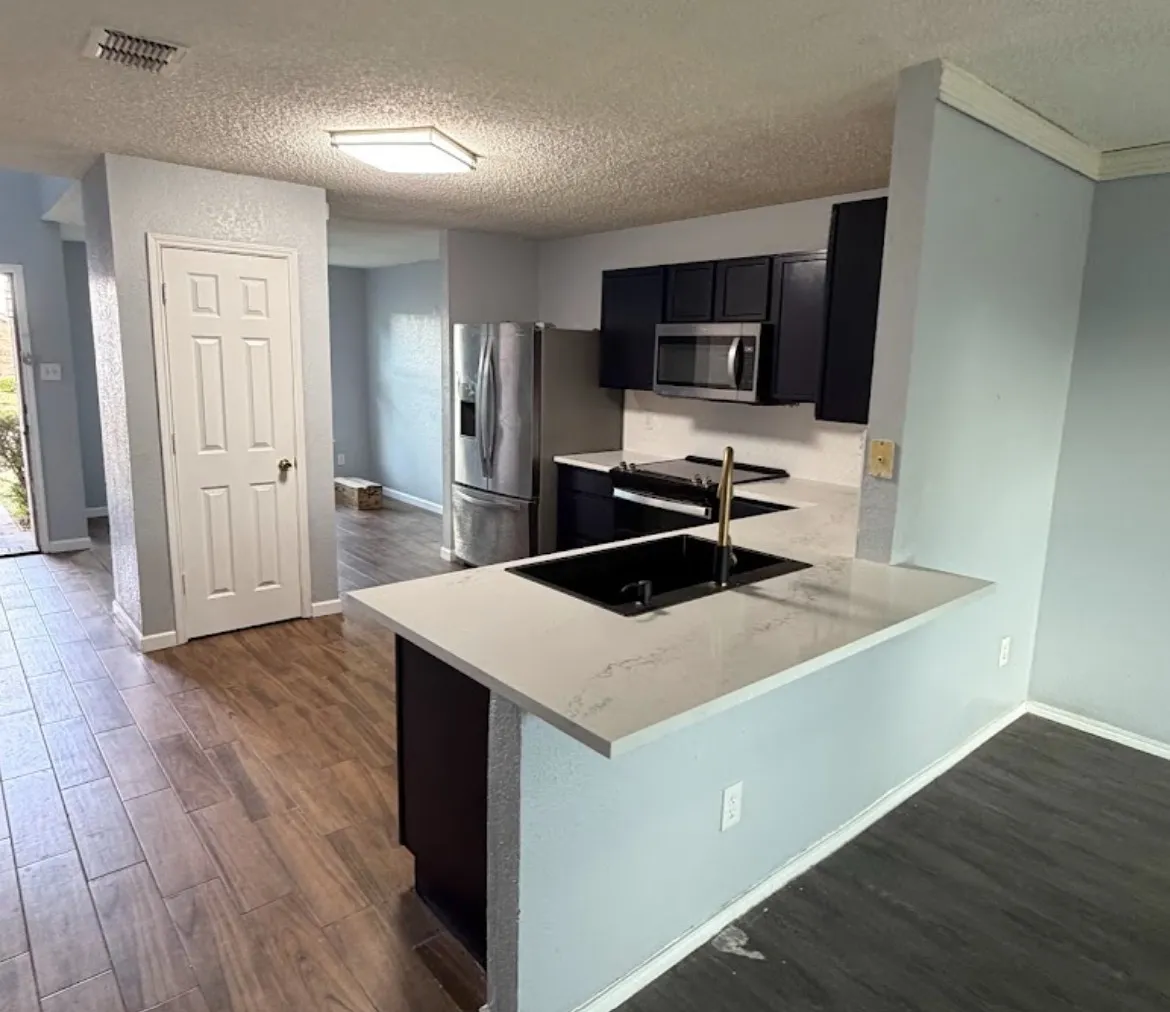 Modern kitchen featuring dark cabinetry, stainless steel appliances, a black sink with a gold-tone faucet, and light-colored countertops