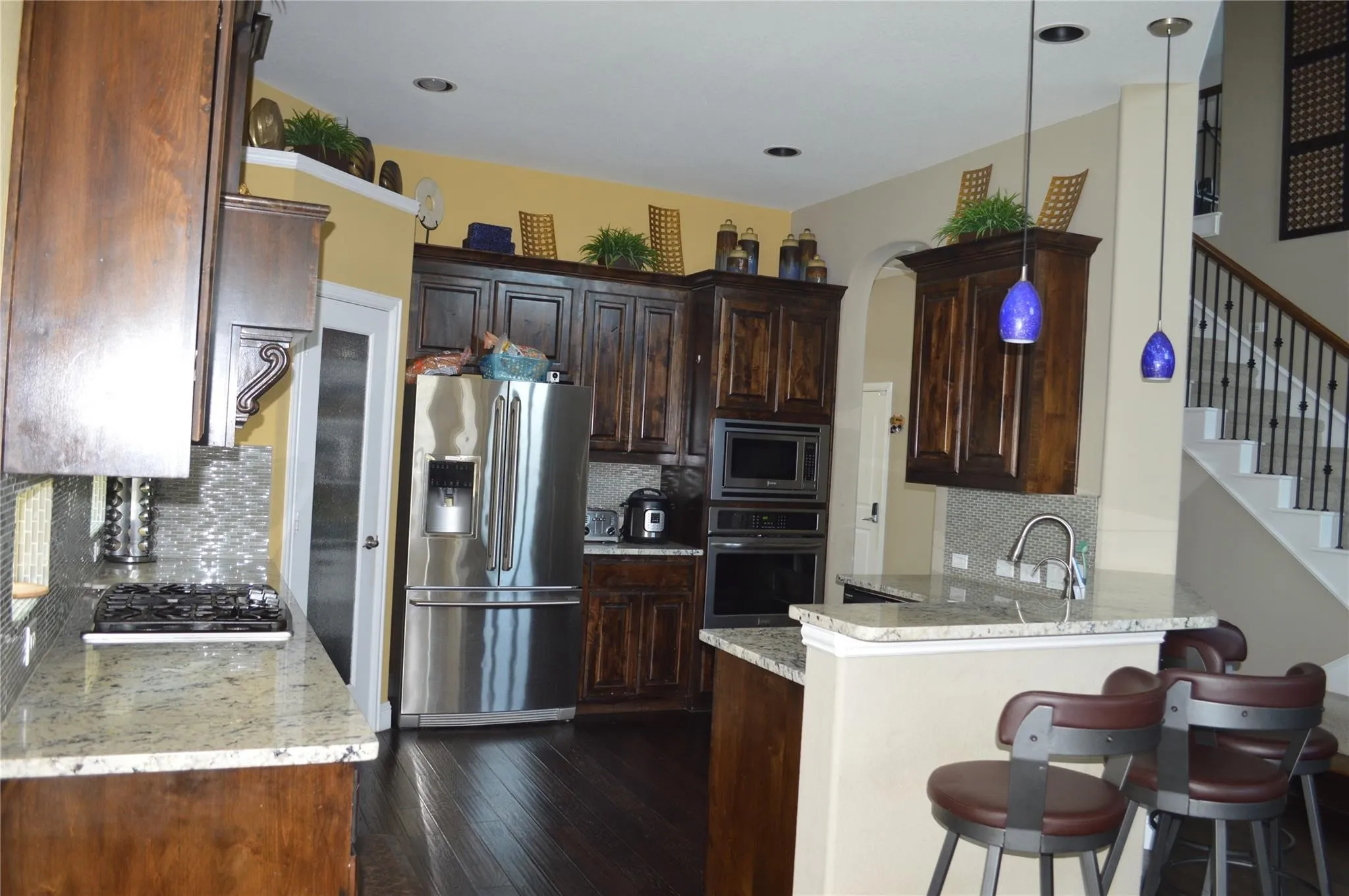 Kitchen with appliances with stainless steel finishes, decorative backsplash, a peninsula, dark wood-type flooring, and light stone countertops