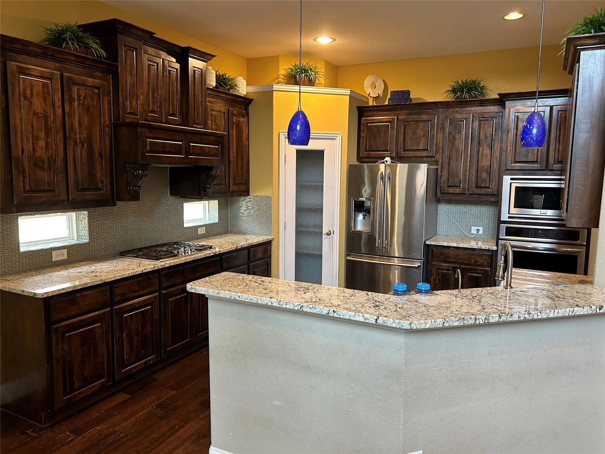 Kitchen featuring dark wood finished floors, appliances with stainless steel finishes, dark brown cabinetry, light stone countertops, and recessed lighting