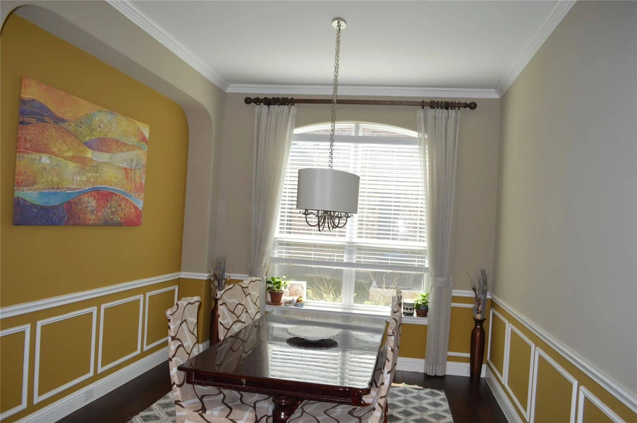 Dining space with dark wood-style floors, ornamental molding, a wainscoted wall, and a decorative wall
