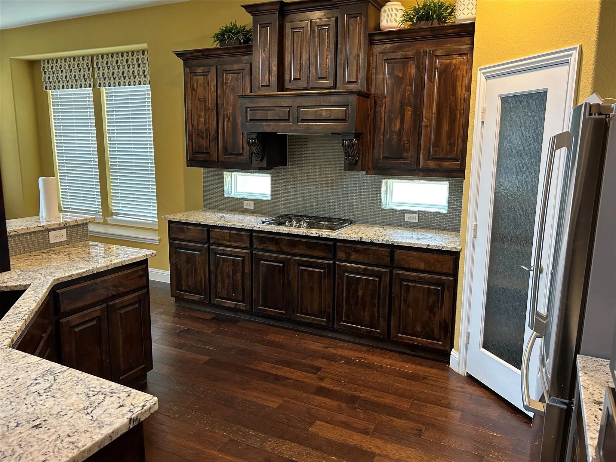 Kitchen featuring dark wood-style flooring, appliances with stainless steel finishes, backsplash, dark brown cabinetry, and light stone counters