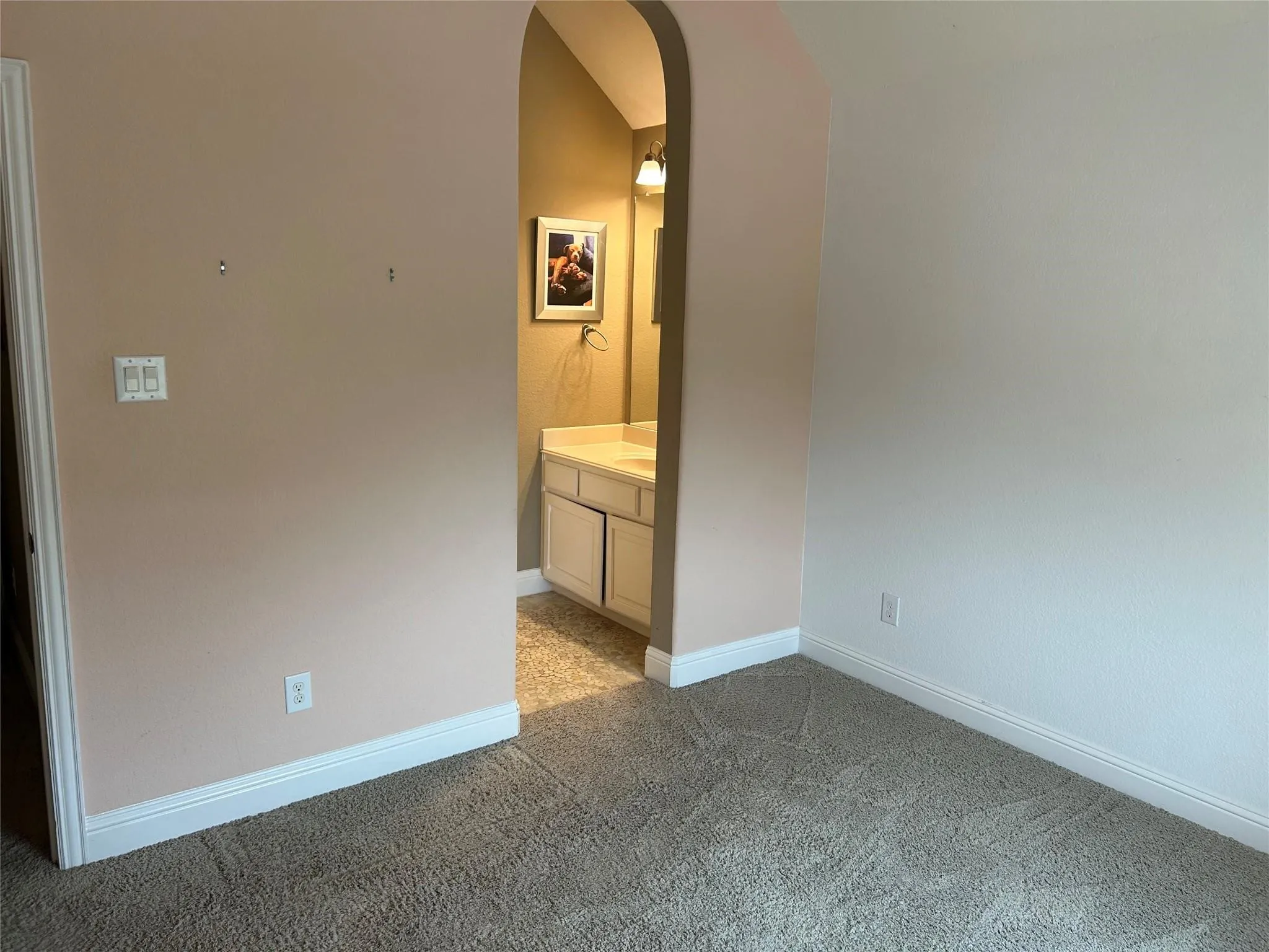 Unfurnished bedroom with arched walkways, light carpet, and connected bathroom