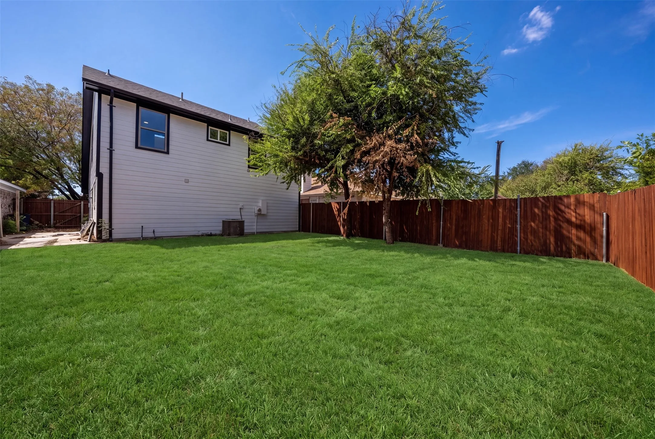 Expansive green lawn, wood fence, white siding, and black-framed window