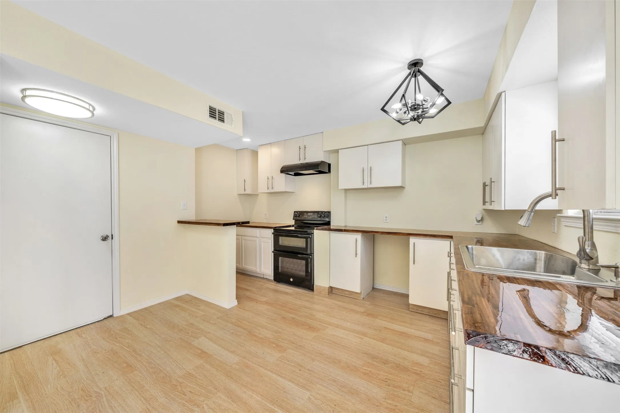 Kitchen featuring wood-finish flooring, white cabinetry, a black range with an overhead hood, and a stainless steel sink