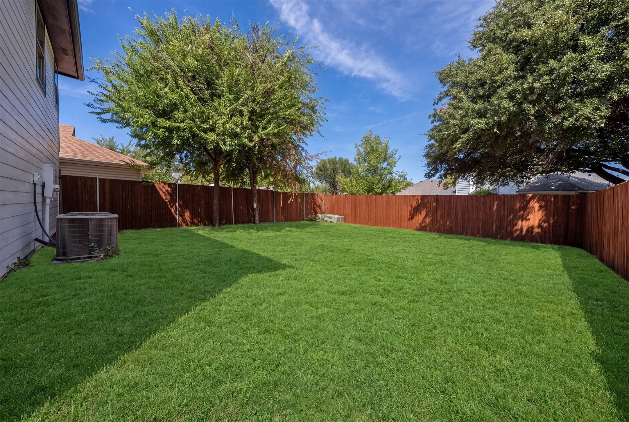 Expansive backyard featuring a manicured lawn, established trees, and a privacy fence