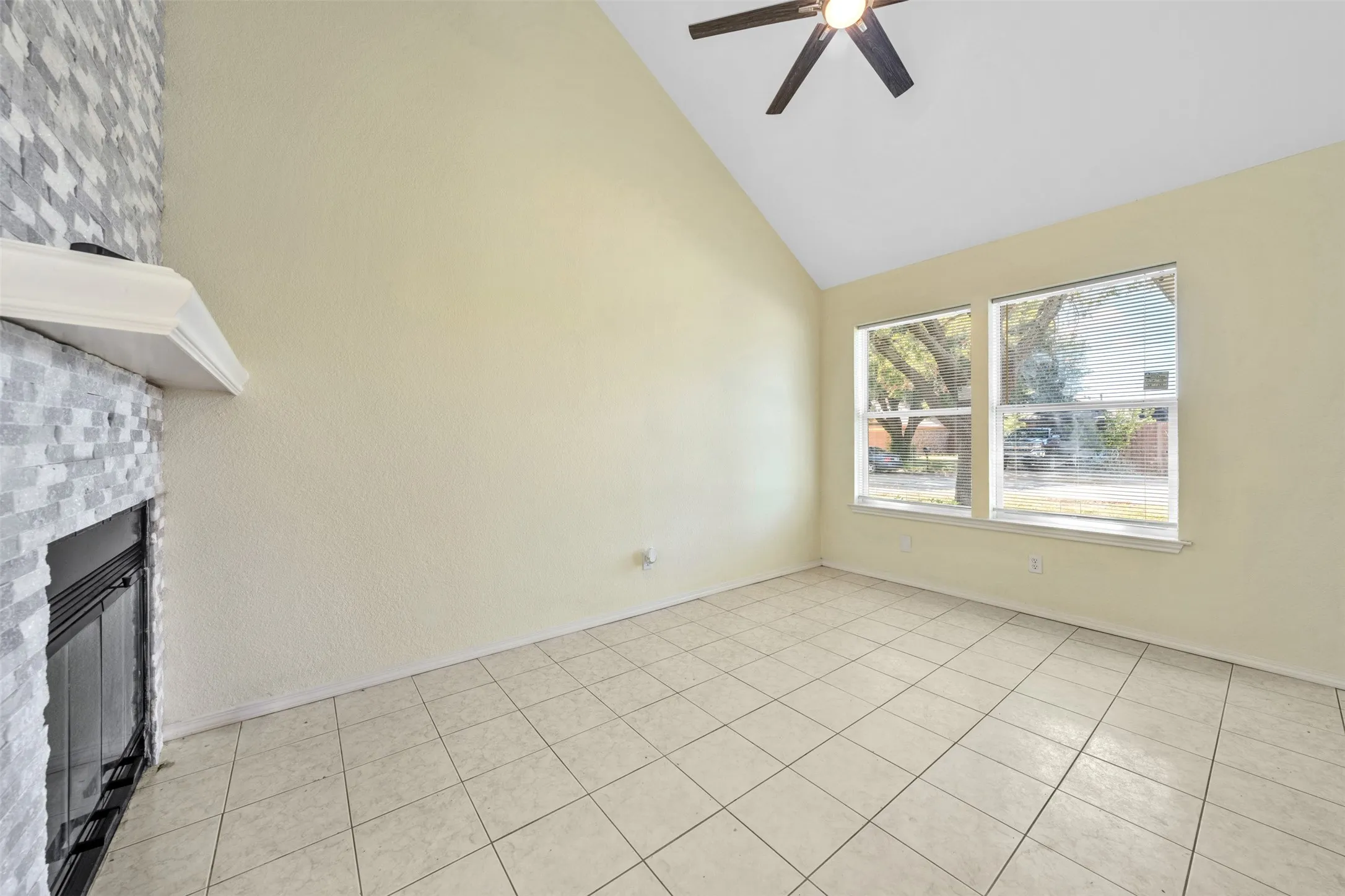 Vaulted ceiling, ceramic tile flooring, two large windows, ceiling fan, and a fireplace with a tile surround