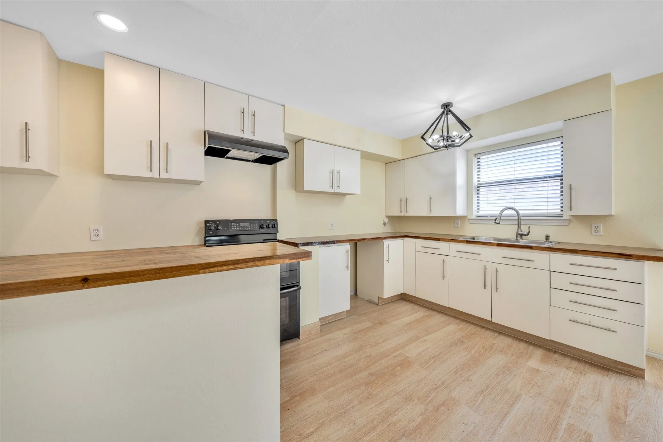 Kitchen featuring ample white cabinetry, wood-finish countertops, stainless steel sink, and wood-finish flooring