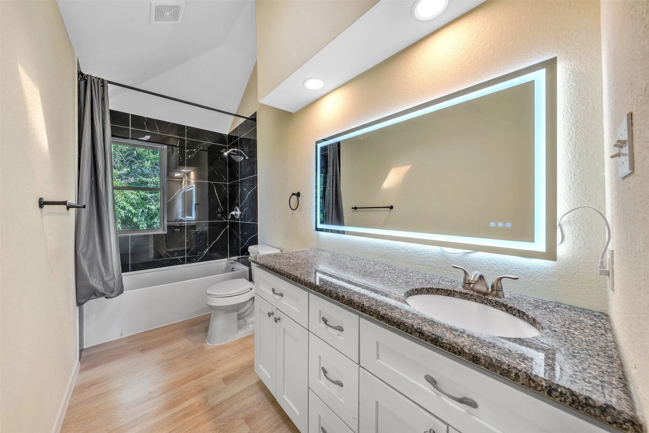 Wood-finish flooring, white vanity with granite-style countertop, integrated sink, and an illuminated mirror