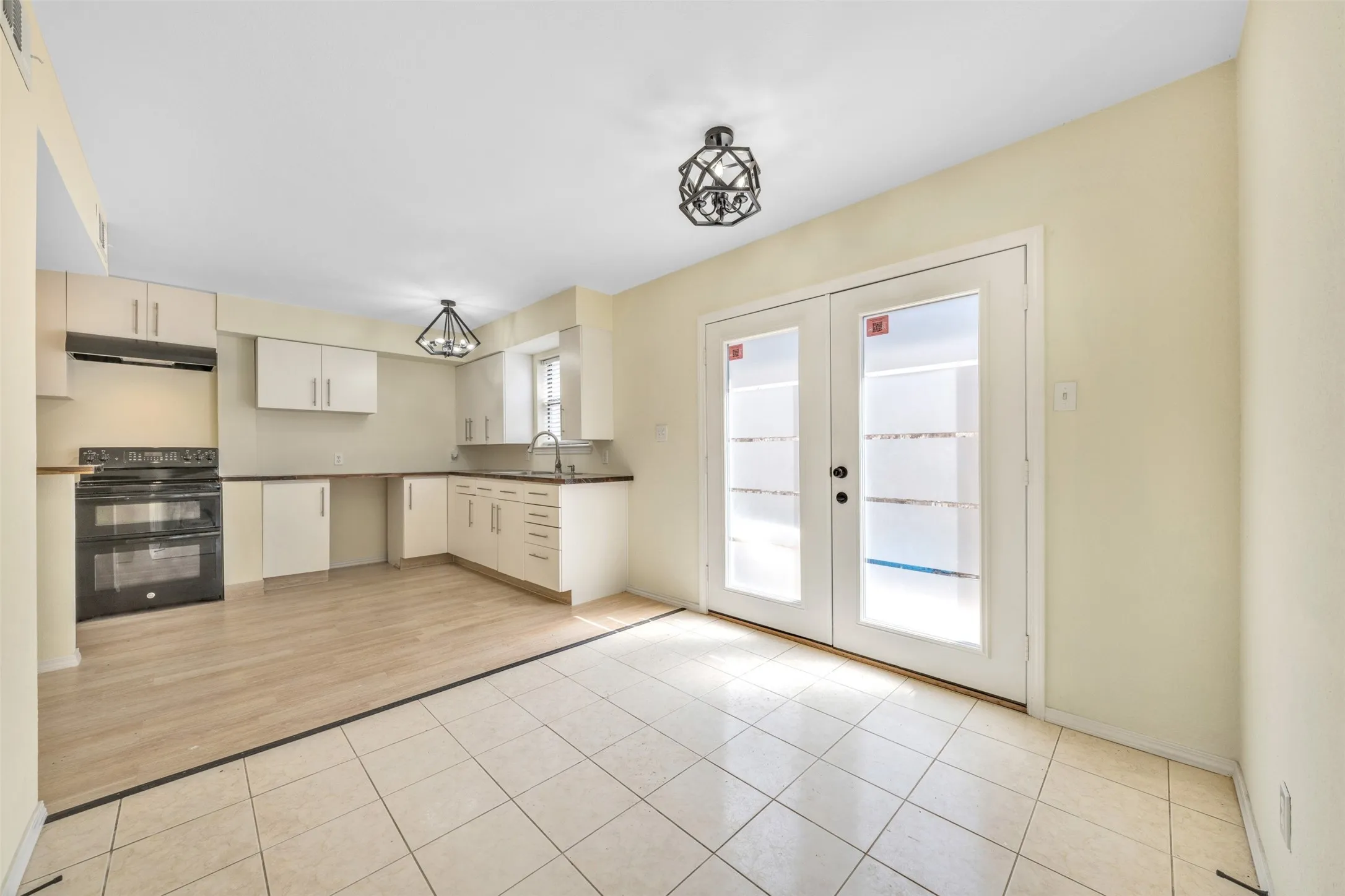 Cream-colored cabinetry, dark countertops, black range with double ovens, wood-finish flooring, and white tile flooring