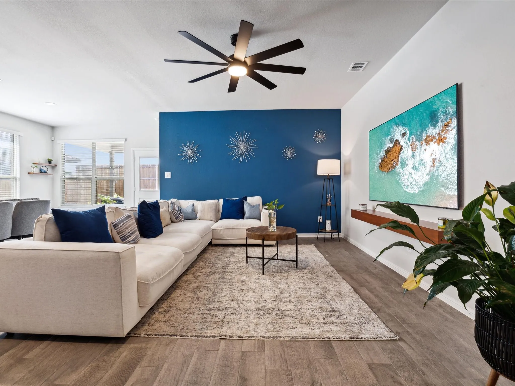 Wood-finish flooring throughout, featuring a distinctive accent wall, ceiling fan with integrated lighting, and a built-in floating shelf