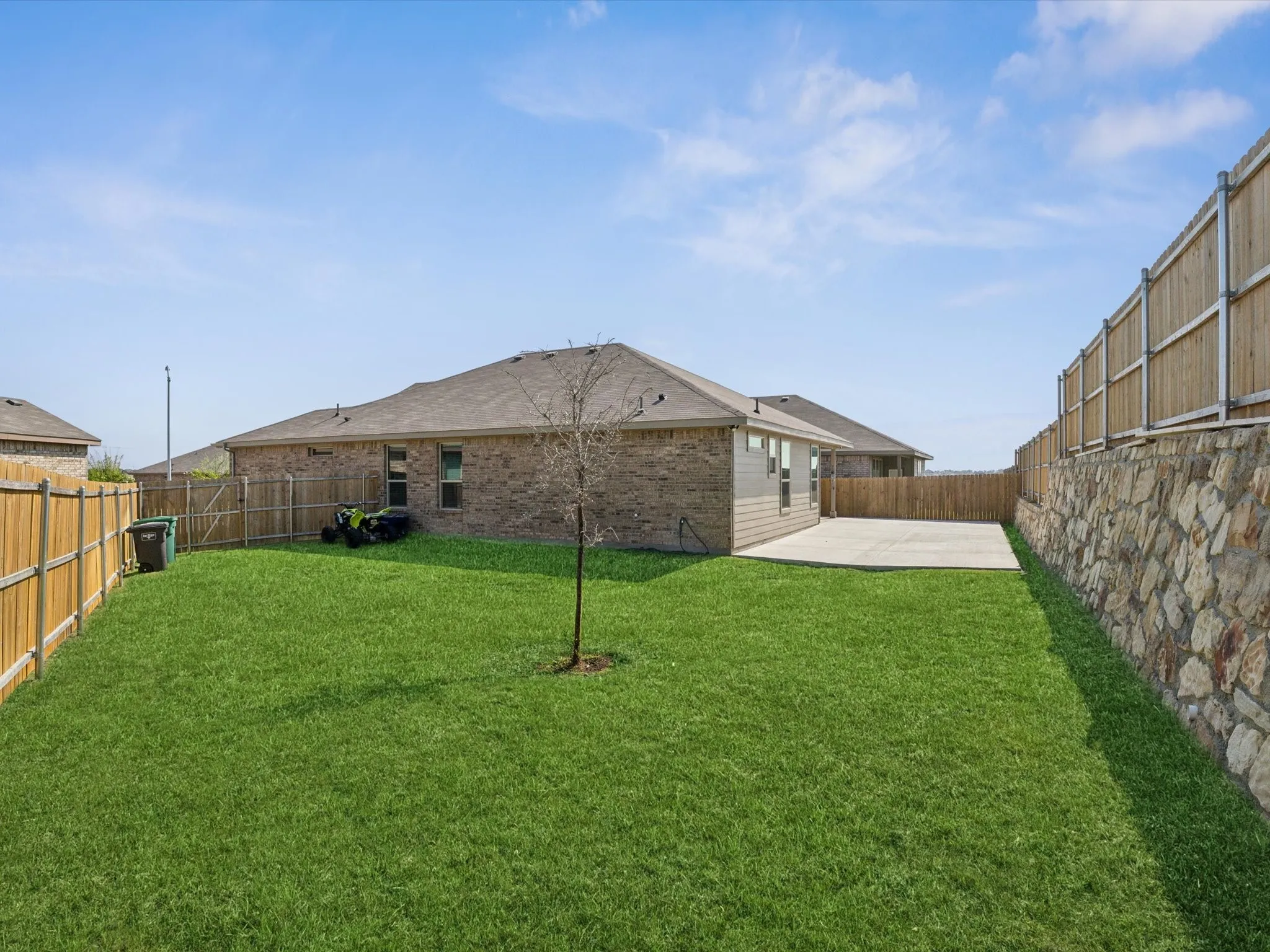 Expansive backyard featuring a stone retaining wall, wood fencing, and a concrete patio