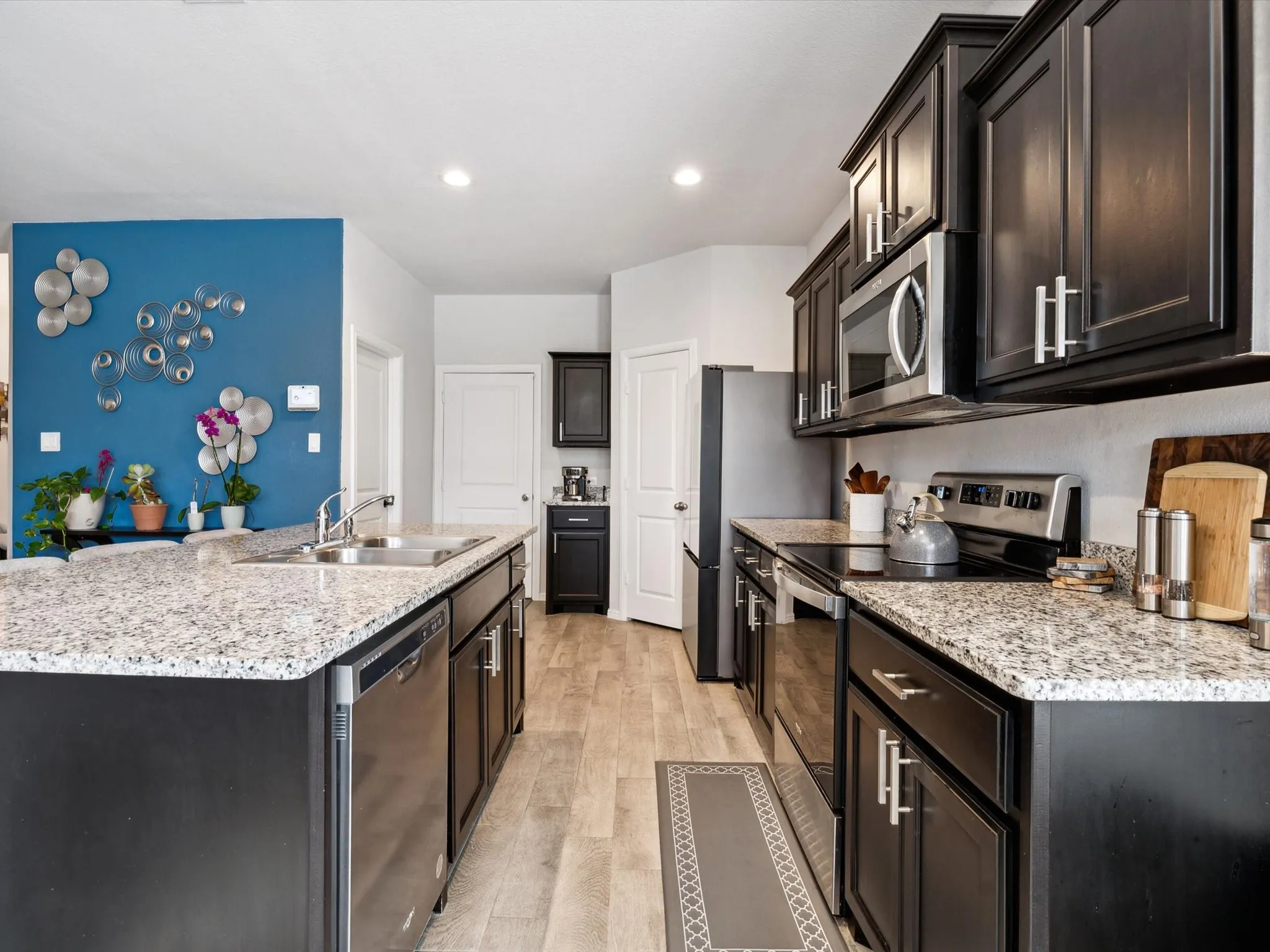 Kitchen featuring an island with a stainless steel sink, dark wood cabinetry, light-toned countertops, stainless steel appliances, and wood-finish flooring