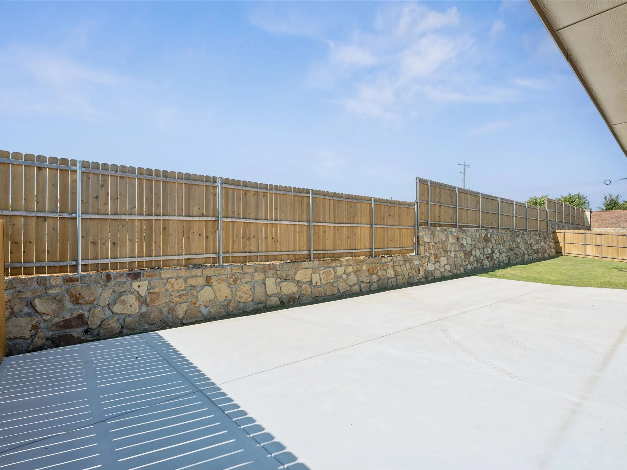 Expansive concrete patio area with a stone-faced retaining wall, wooden privacy fence, and a section of green lawn