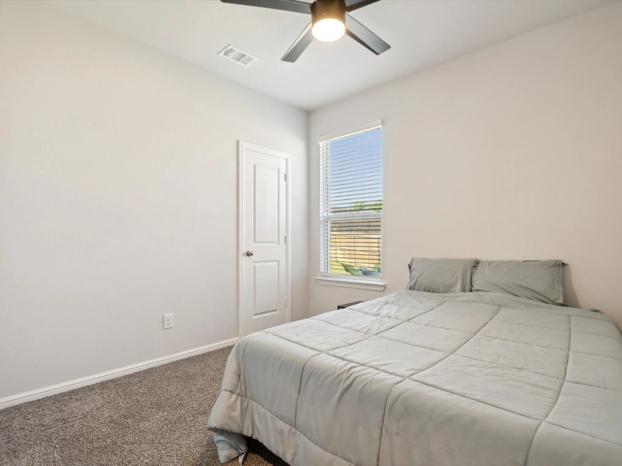 Neutral wall colors, textured carpeting, contemporary ceiling fan, and a single window with blinds