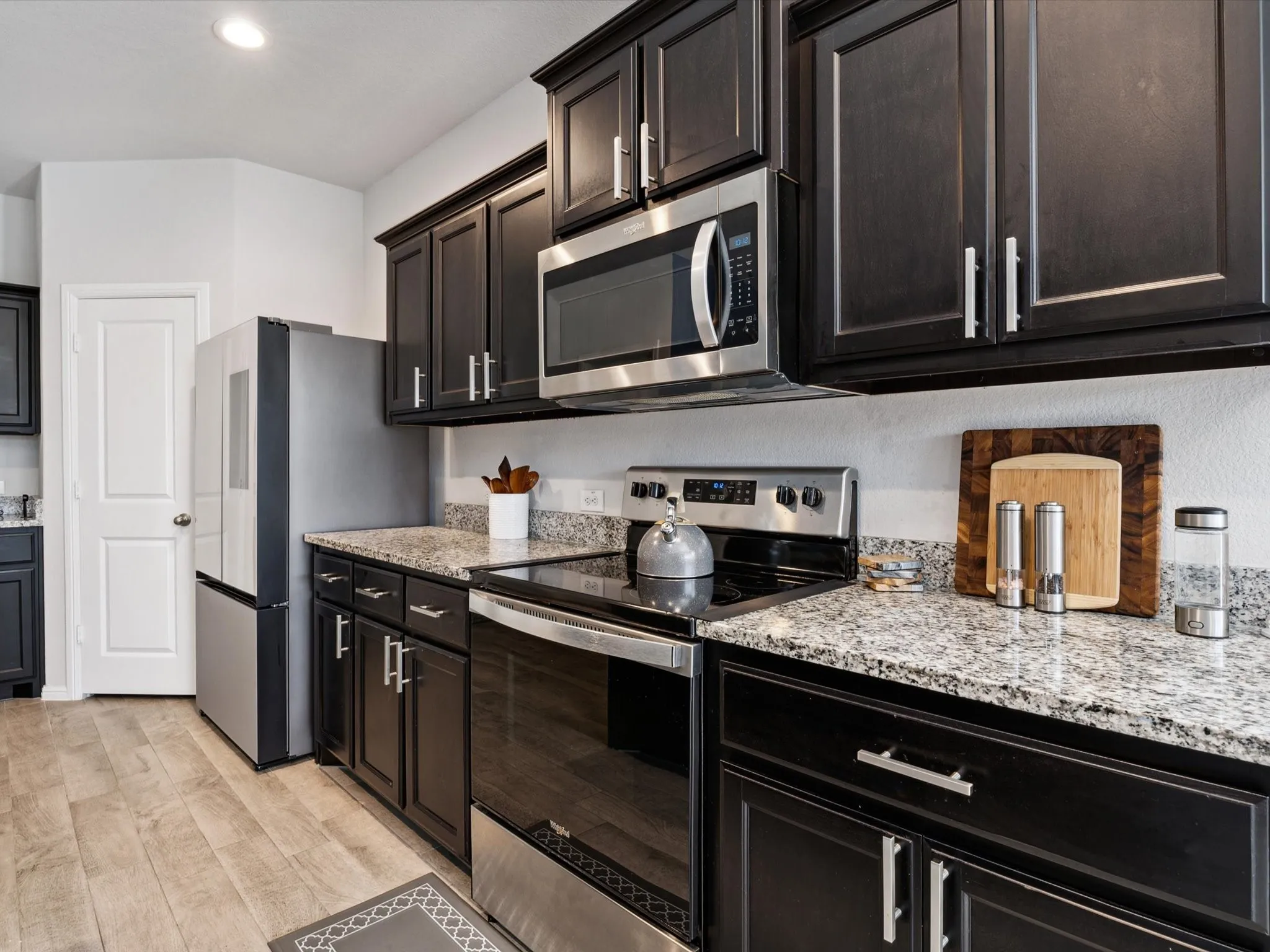 Stainless steel appliances, dark wood-finish cabinetry, light wood-finish flooring, and light-toned countertops