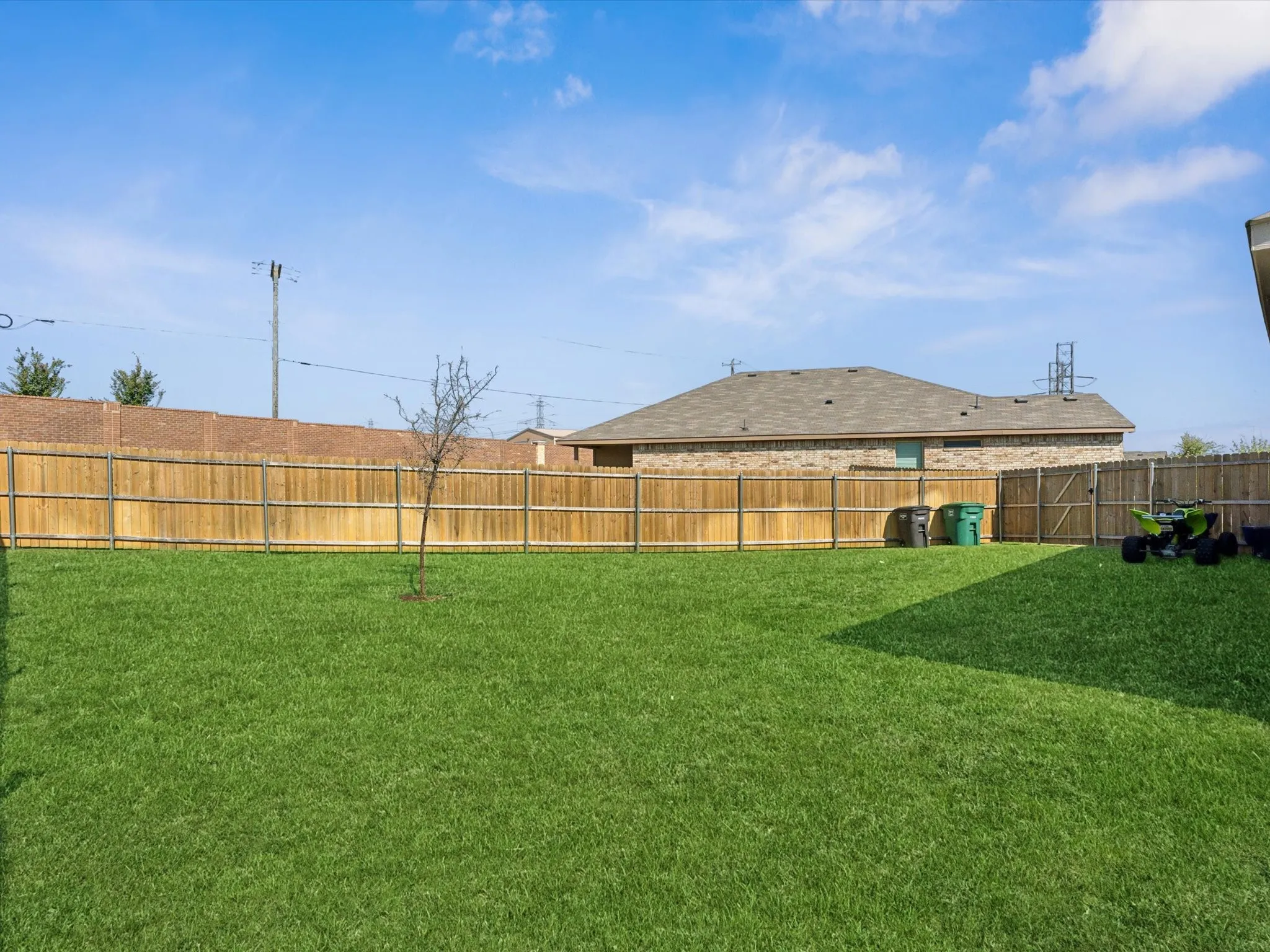 Expansive backyard featuring a lush lawn, wood panel fencing, and a small tree