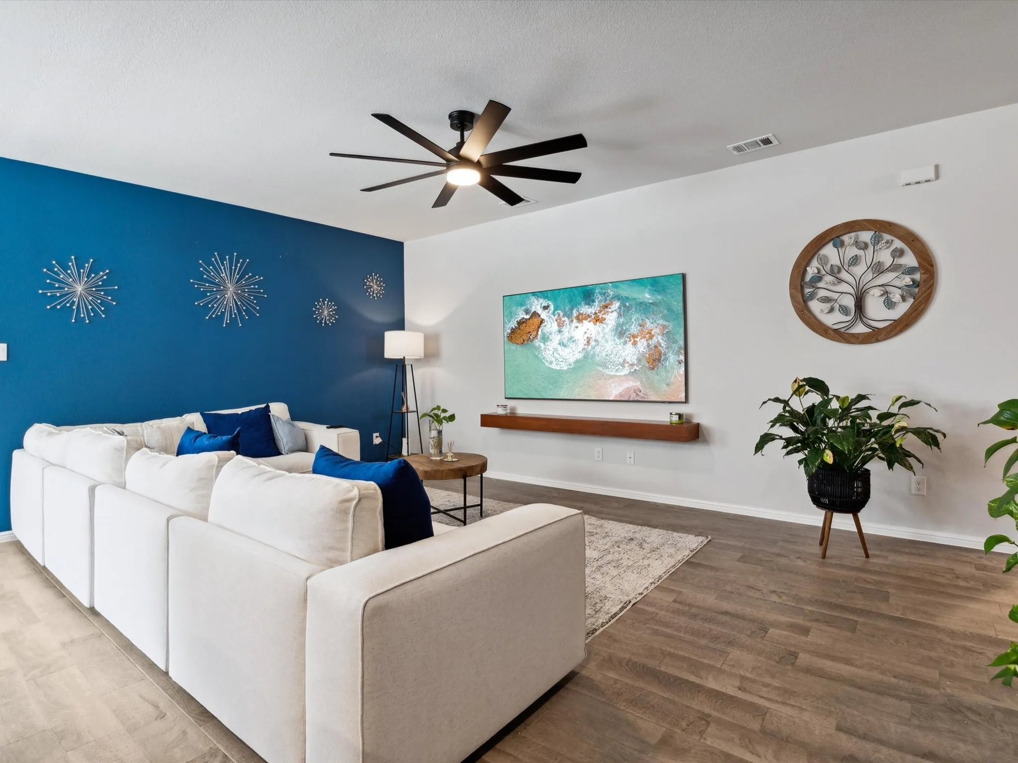Wood-finish flooring throughout, ceiling fan with integrated lighting, and a floating wood-tone shelf