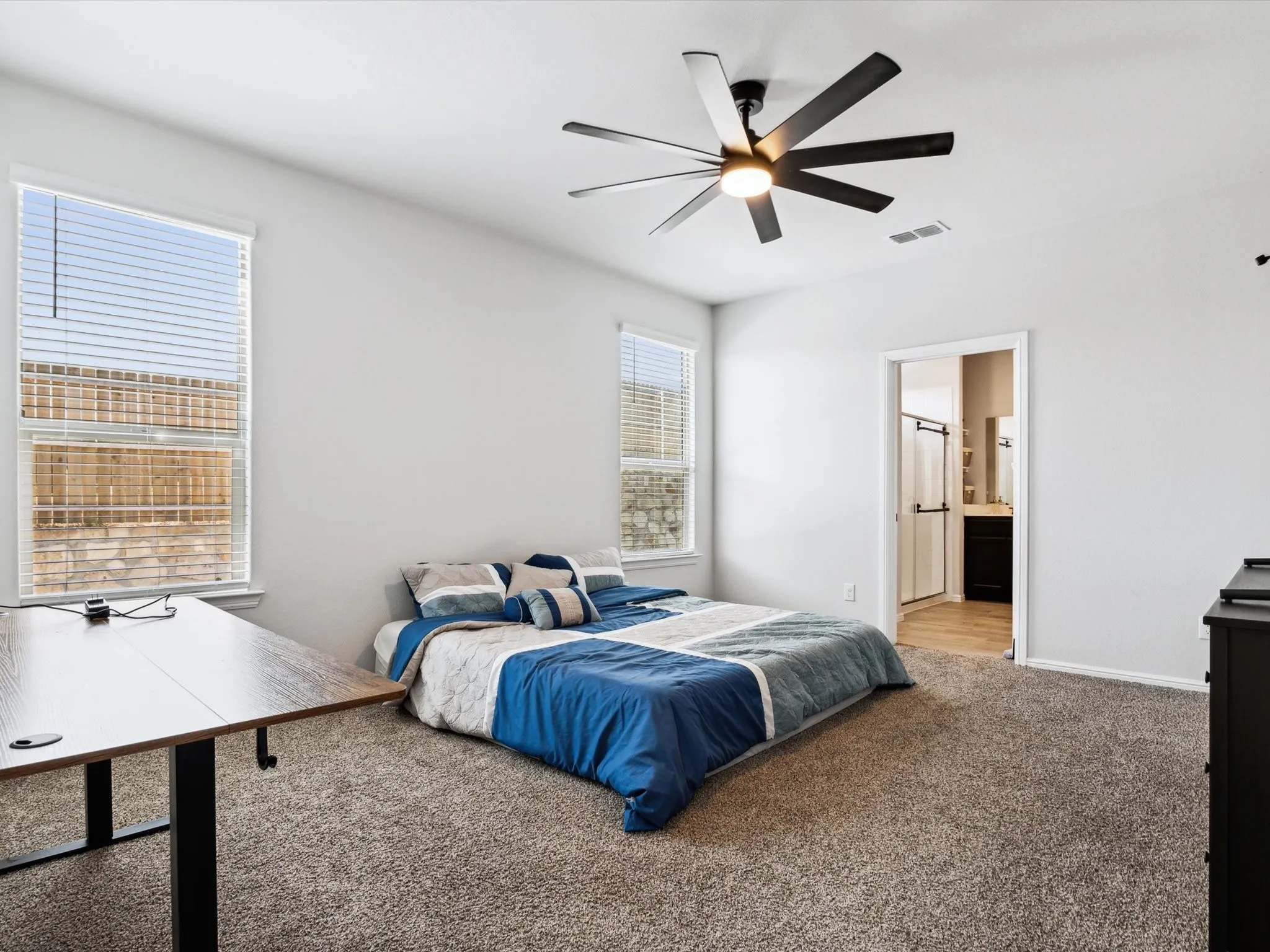 Spacious room with plush carpeting, two windows with blinds, and a contemporary ceiling fan