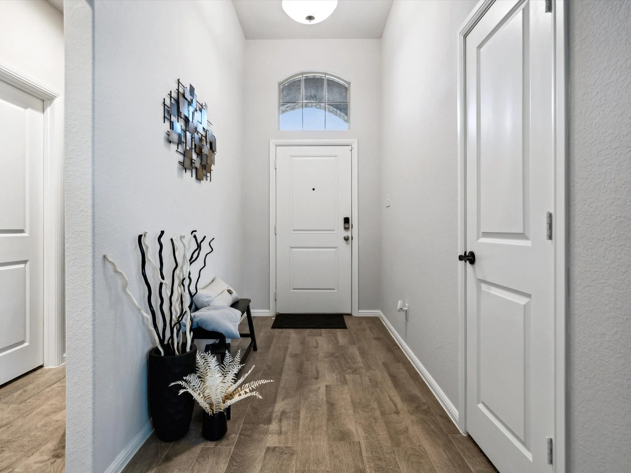 Entryway featuring wood-finish flooring, white panel doors, and an arched transom window above the main entry