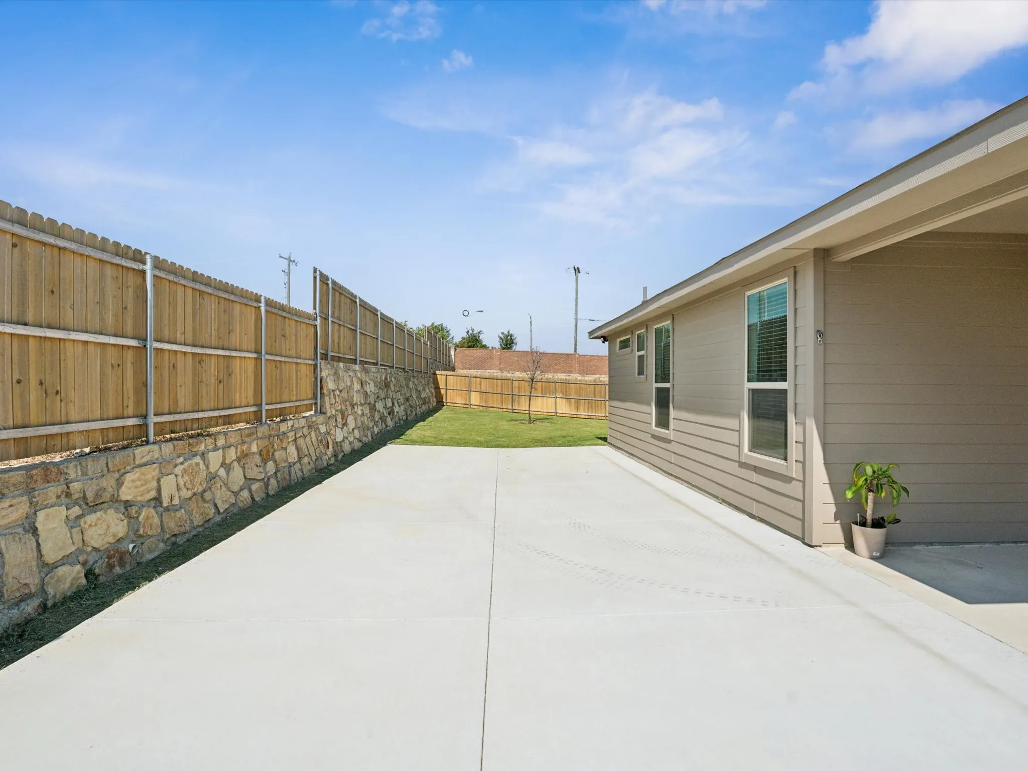 Exterior featuring beige siding, multiple windows, a concrete driveway, and a wood privacy fence with a stone retaining wall