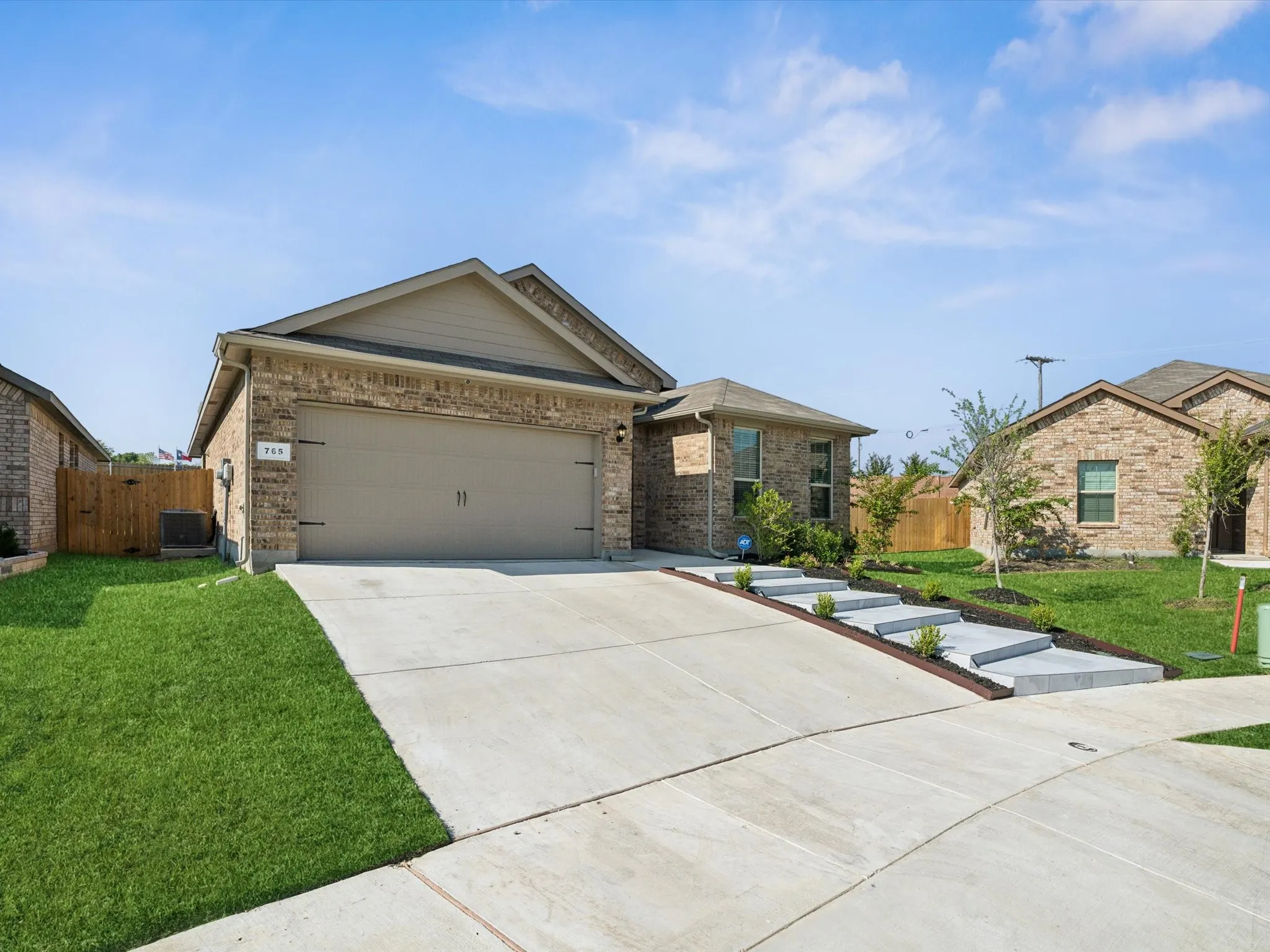 Brick veneer exterior with a two-car garage, concrete driveway, landscaped front yard, and a tiered walkway