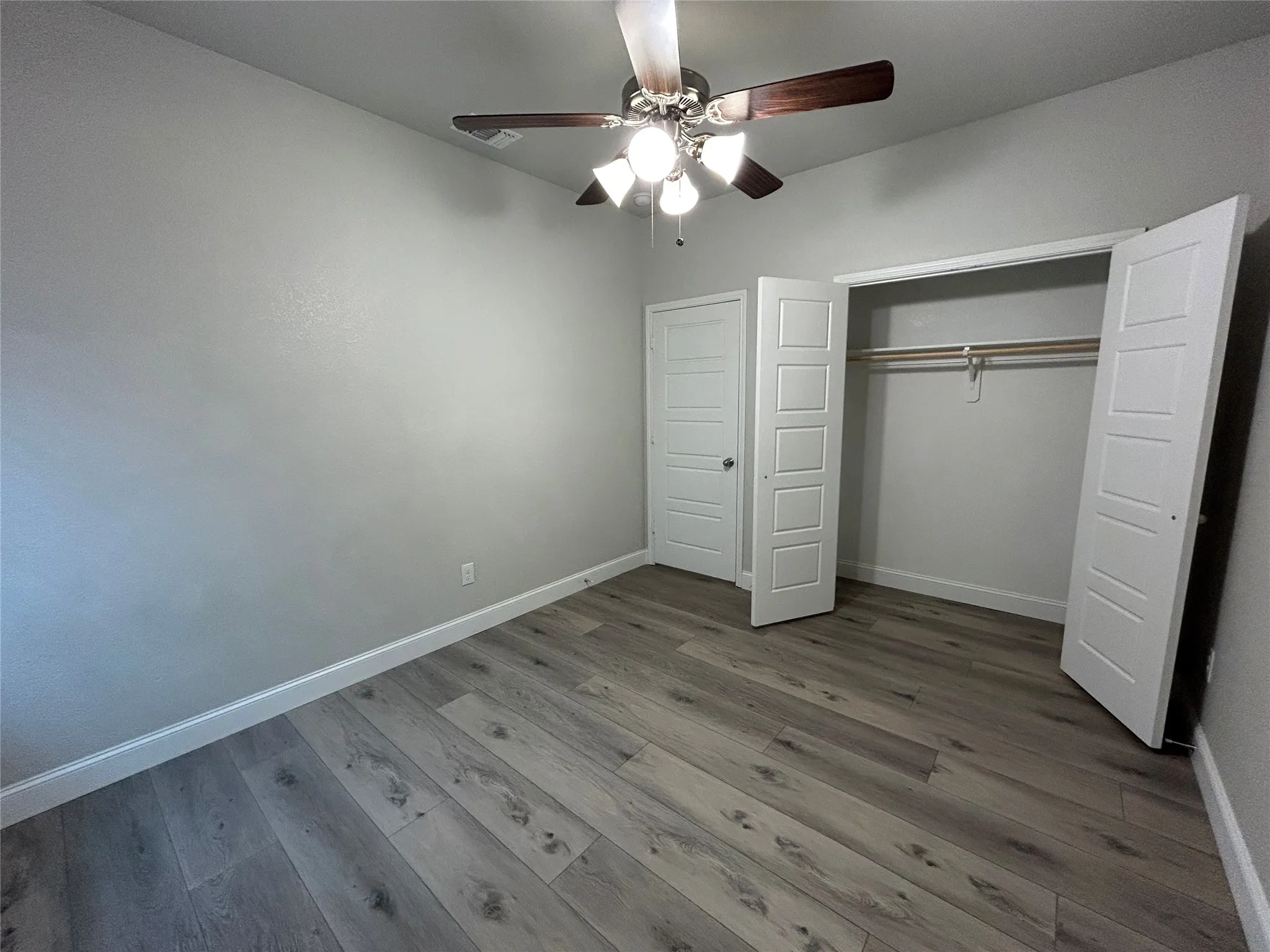 Wood-finish flooring, ceiling fan with light fixture, and a built-in closet with bifold doors