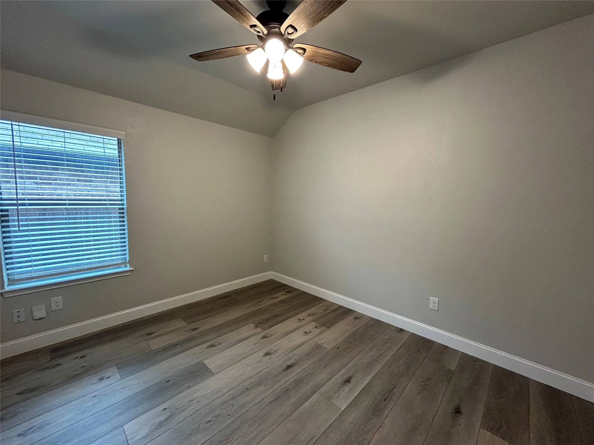 Wood-finish flooring, ceiling fan with light fixture, window with blinds, neutral paint, and white trim