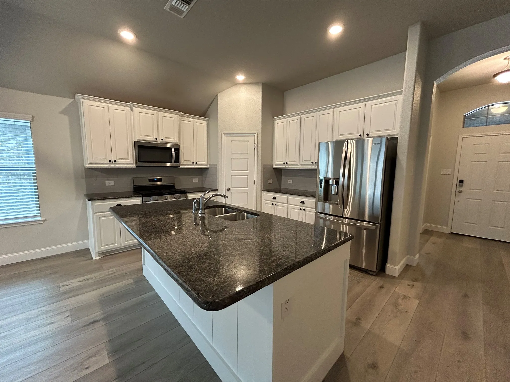 Kitchen with white cabinetry, stainless steel appliances, a dark countertop, and an island featuring an undermount sink