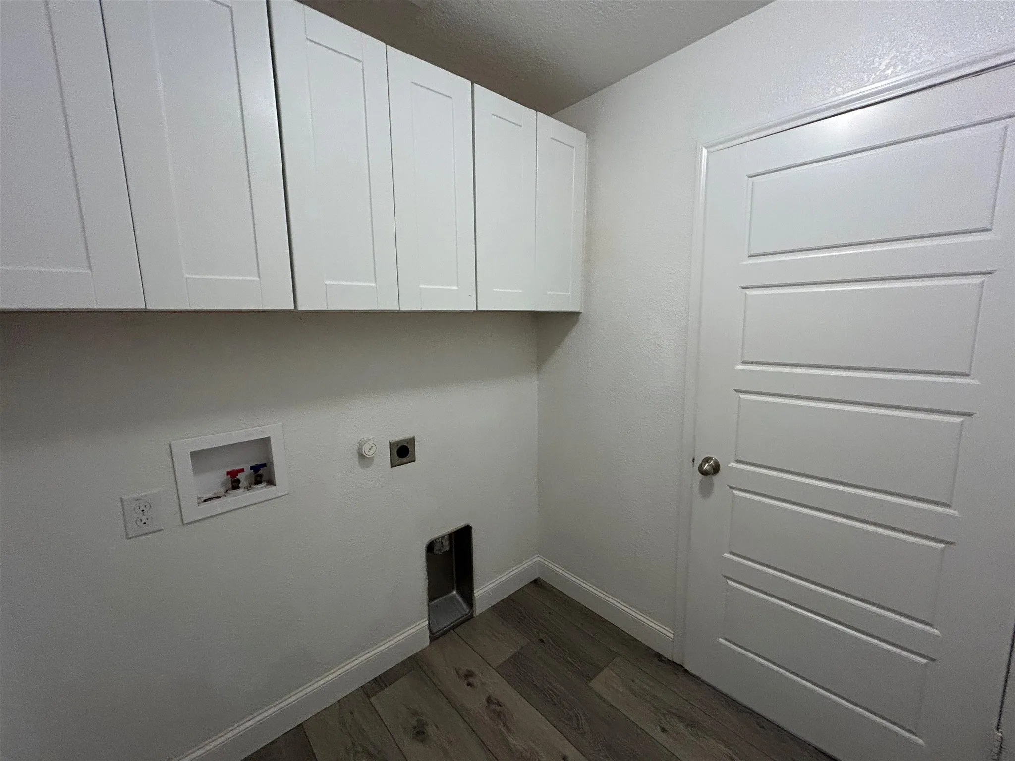 White shaker-style cabinetry, wood-finish flooring, white paneled door, and appliance hookups