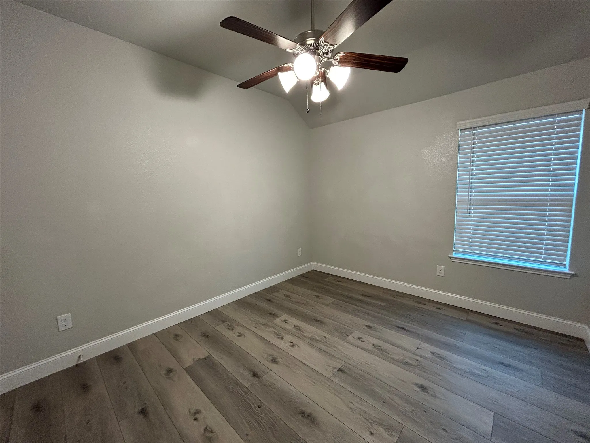 Wood-finish flooring, neutral wall tones, window with horizontal blinds, and a ceiling fan with integrated lighting