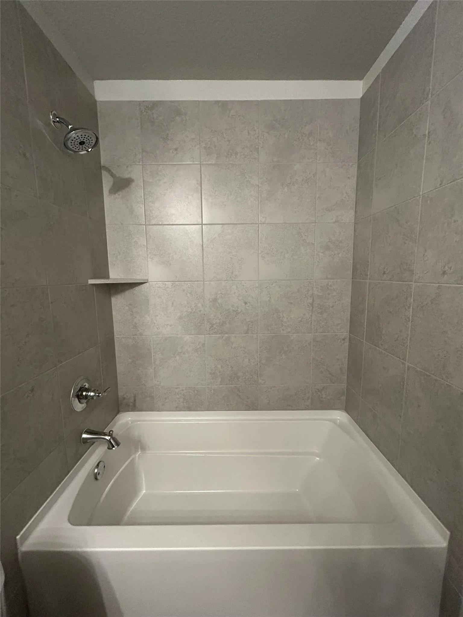 White built-in bathtub with subway tile surround, integrated shower shelf, and chrome fixtures