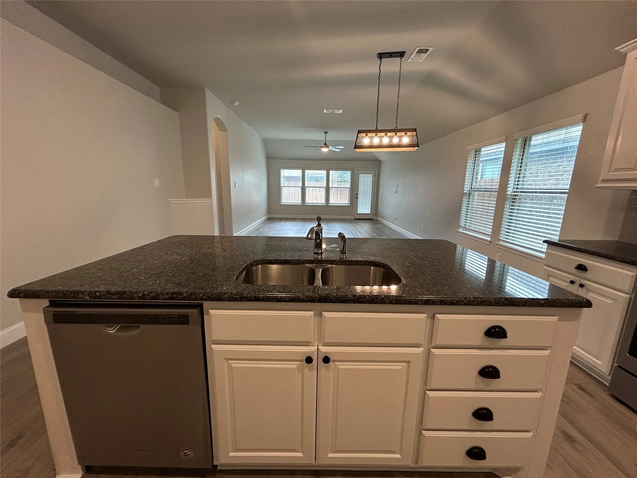 Kitchen island with a granite-style countertop, undermount stainless steel sink, and white cabinetry