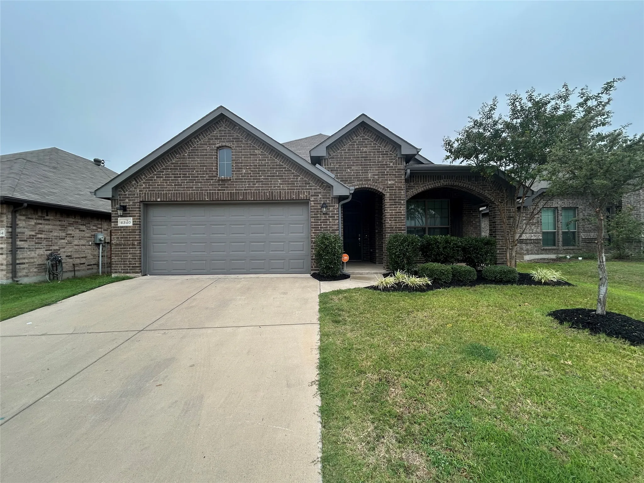Brick exterior with arched entryway, attached garage, and landscaped front yard