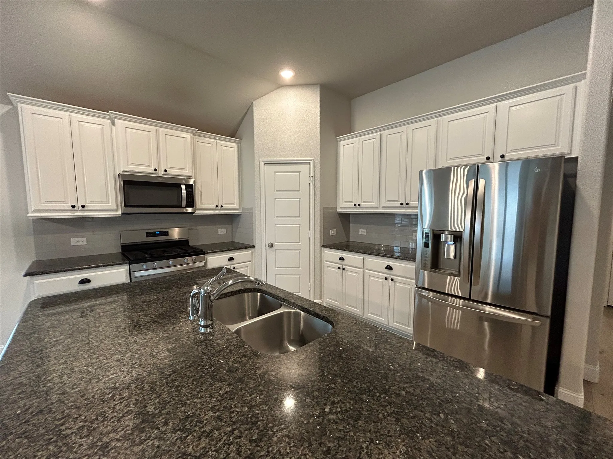 Kitchen featuring an island with a dual basin sink, white cabinetry with dark hardware, stainless steel appliances, and dark countertops