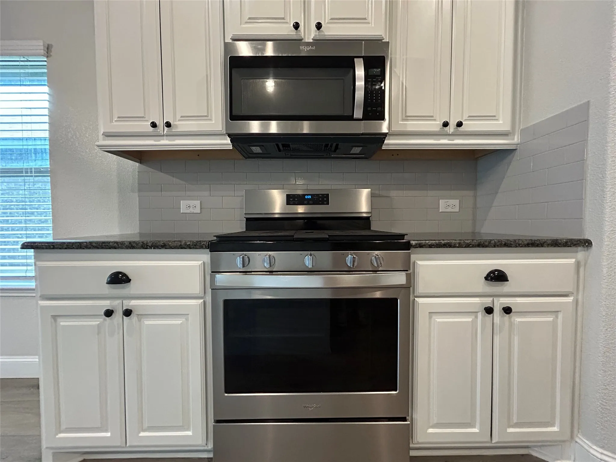 White cabinetry, stainless steel appliances, dark countertops, and a subway tile backsplash