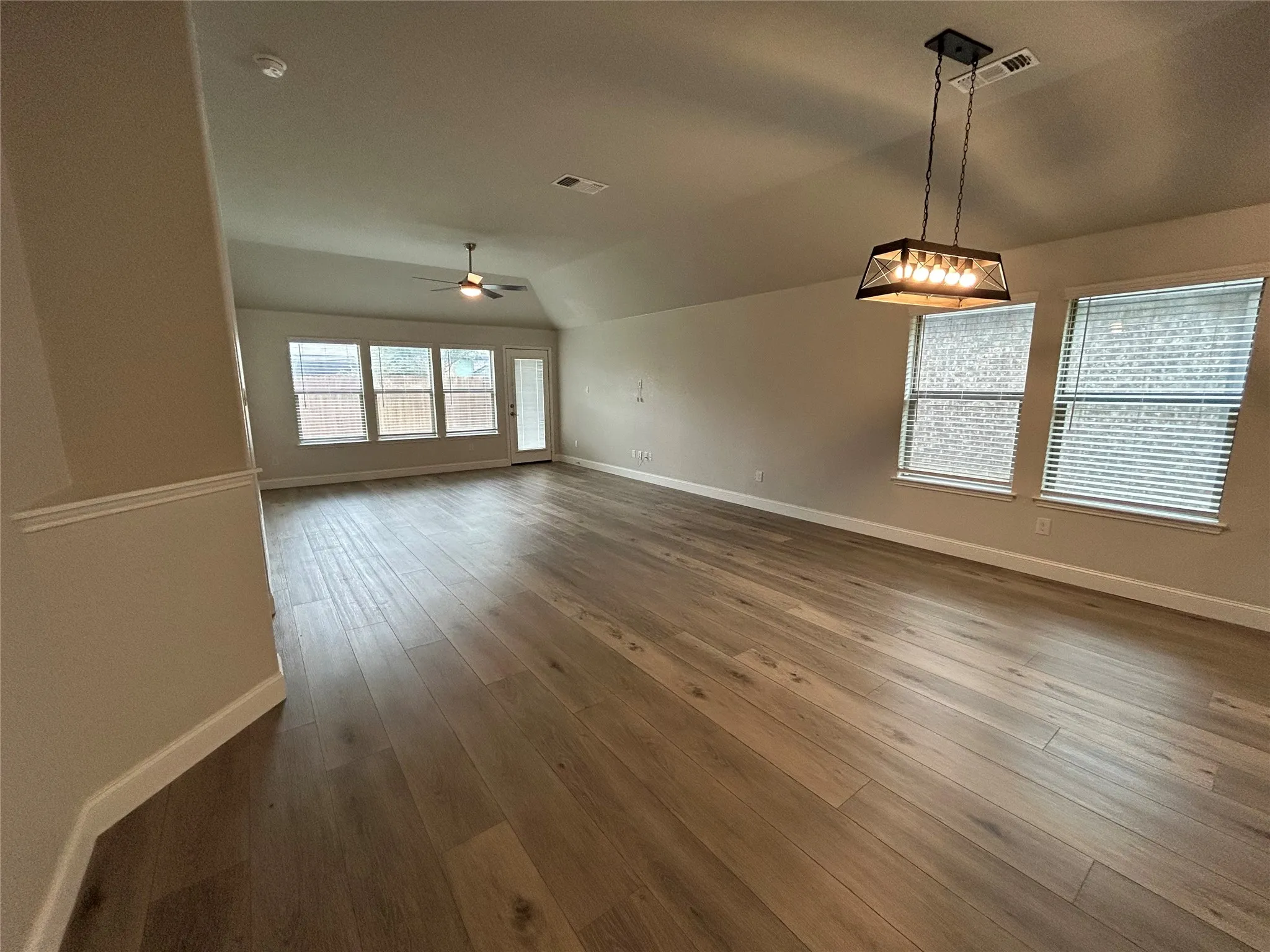 Vaulted ceilings, wood-finish flooring, and multiple windows with blinds