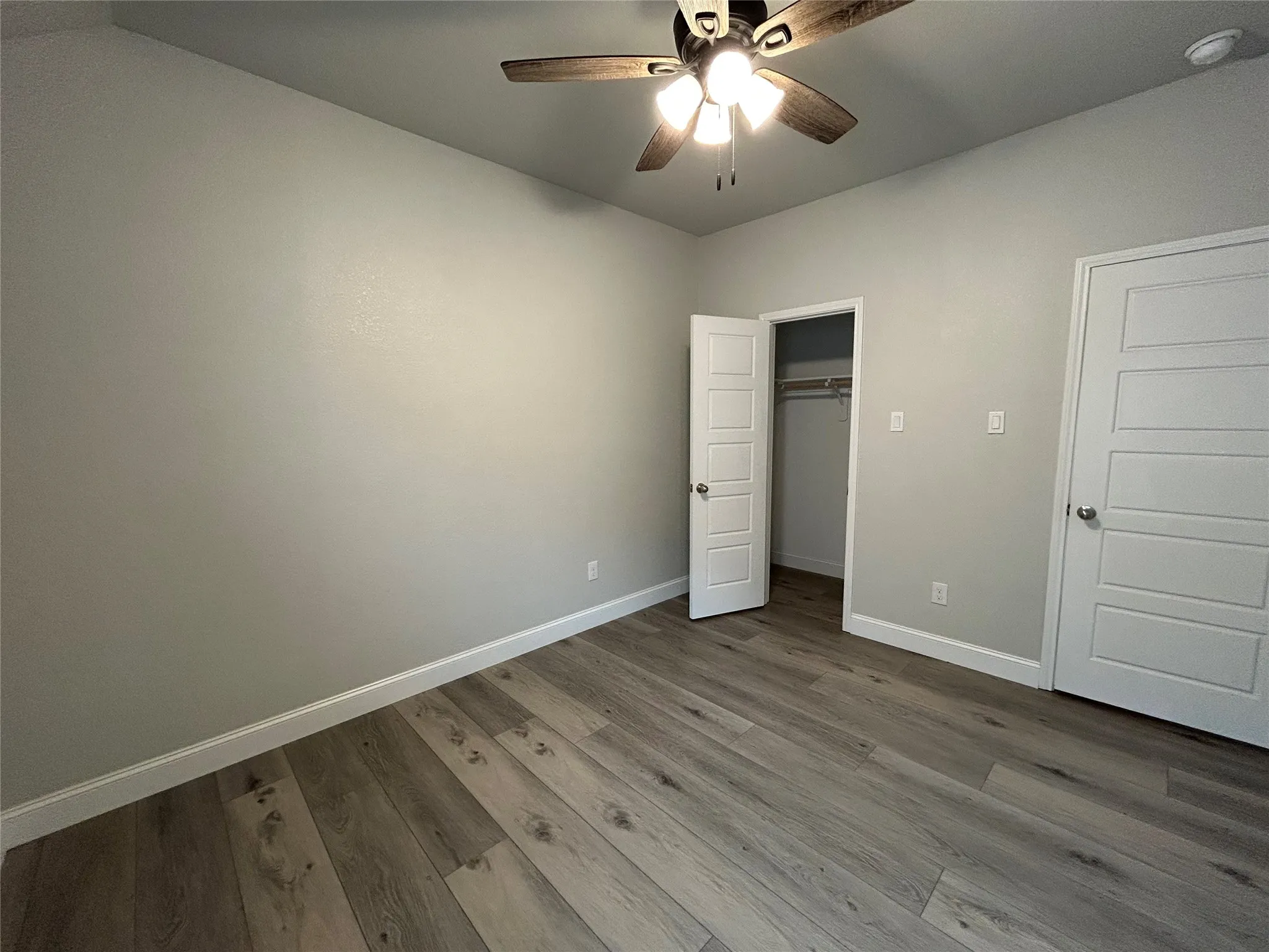 Wood-finish flooring, light grey wall paint, a ceiling fan with integrated lighting, and white paneled doors