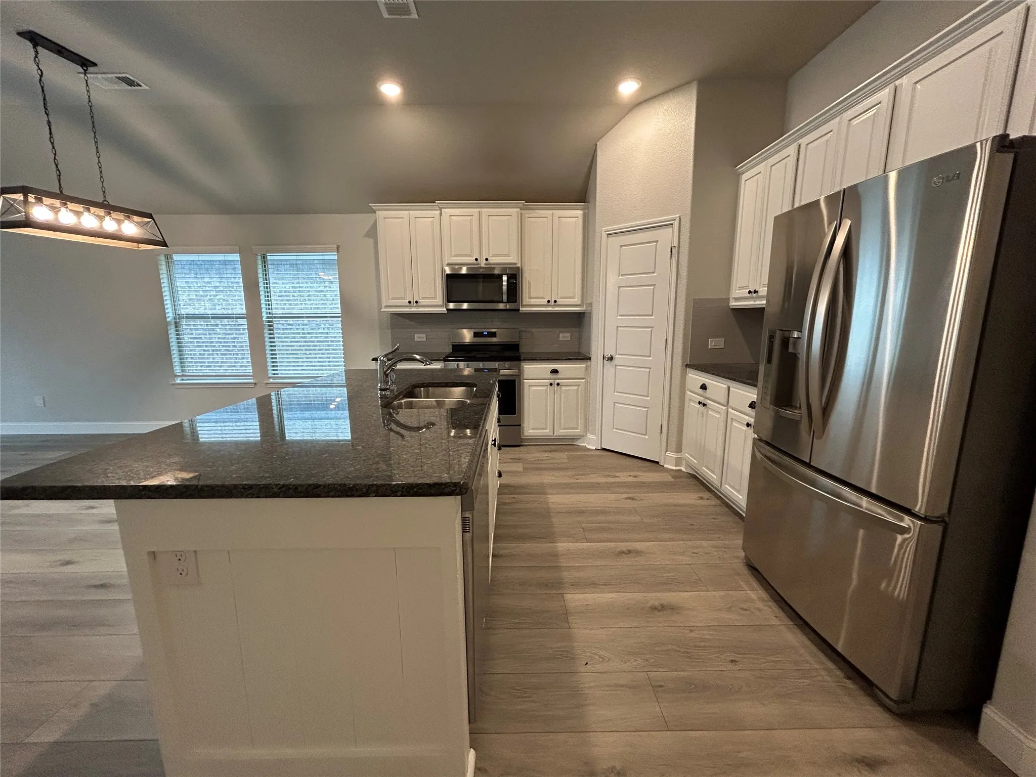 Kitchen featuring a large island with dark stone countertops, stainless steel appliances, wood-finish flooring, white cabinetry, and a contemporary chandelier