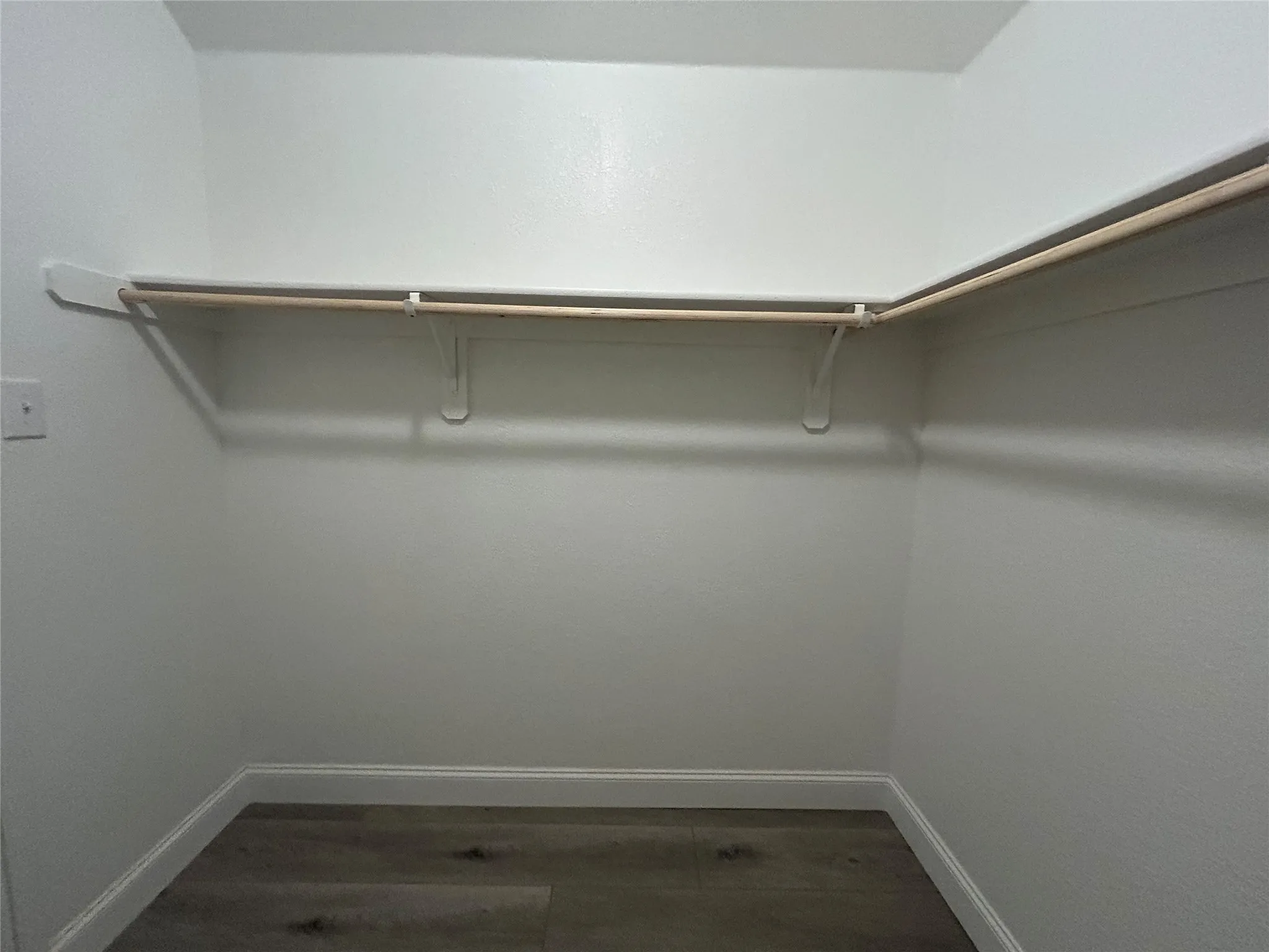 Walk-in closet with L-shaped shelving and wood-finish flooring