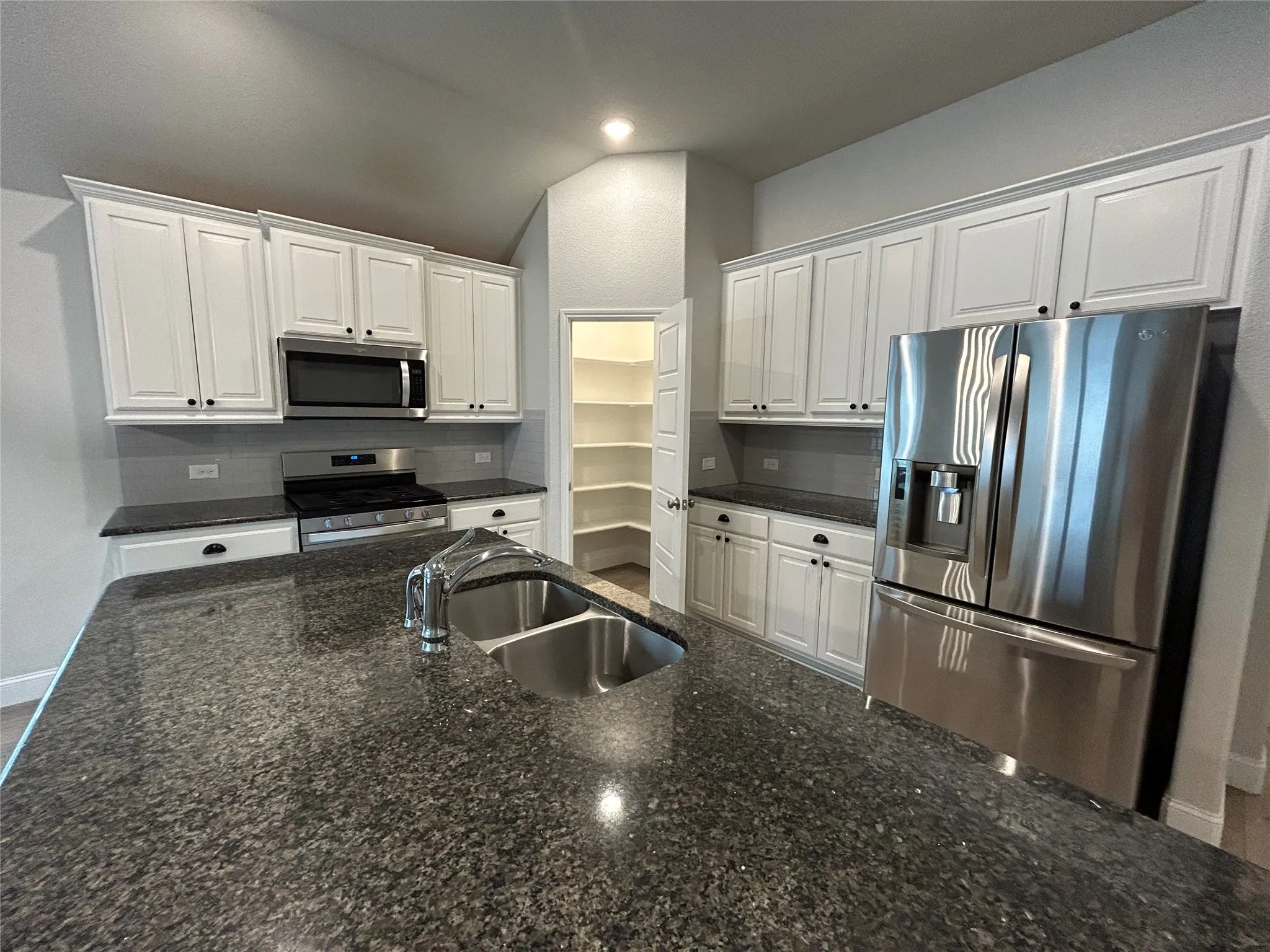 Kitchen featuring an island with a double basin sink, stainless steel appliances, white cabinetry, and granite countertops