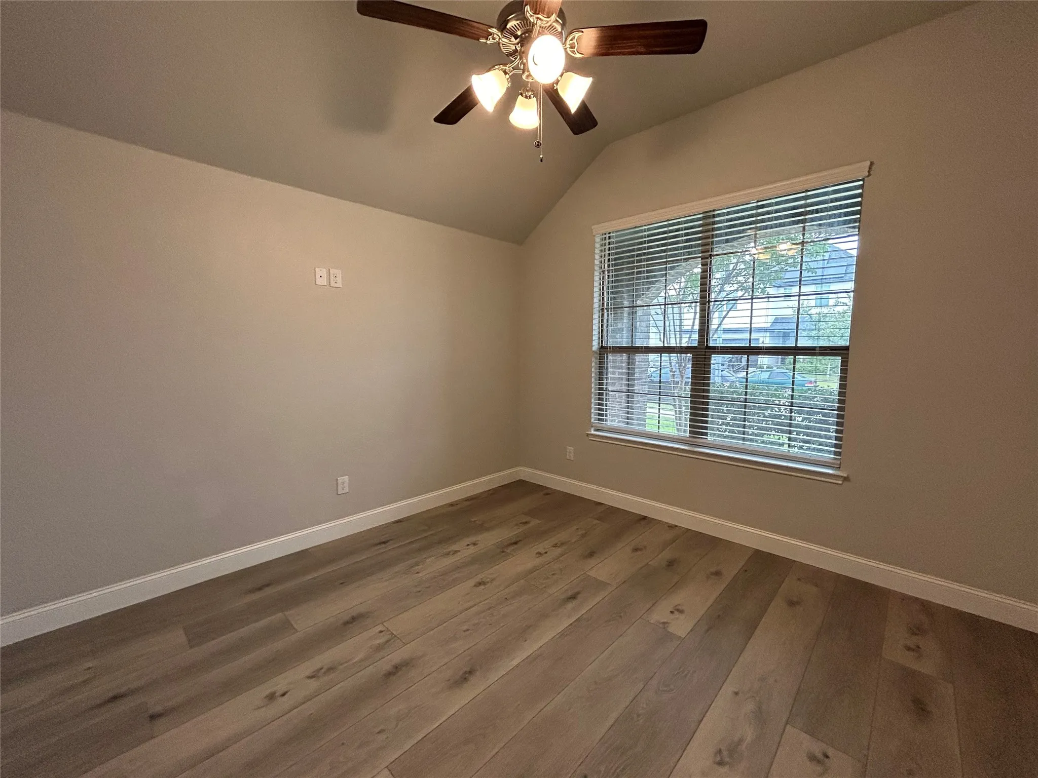 Vaulted ceiling with a ceiling fan light fixture, wood-finish flooring, and a window with blinds