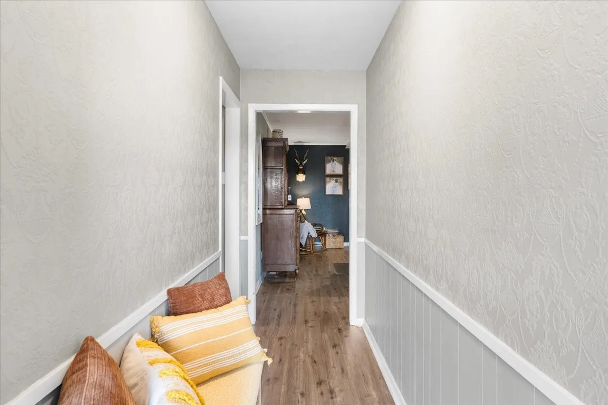 Hallway featuring wood-finish flooring, wainscoting, and textured wall coverings