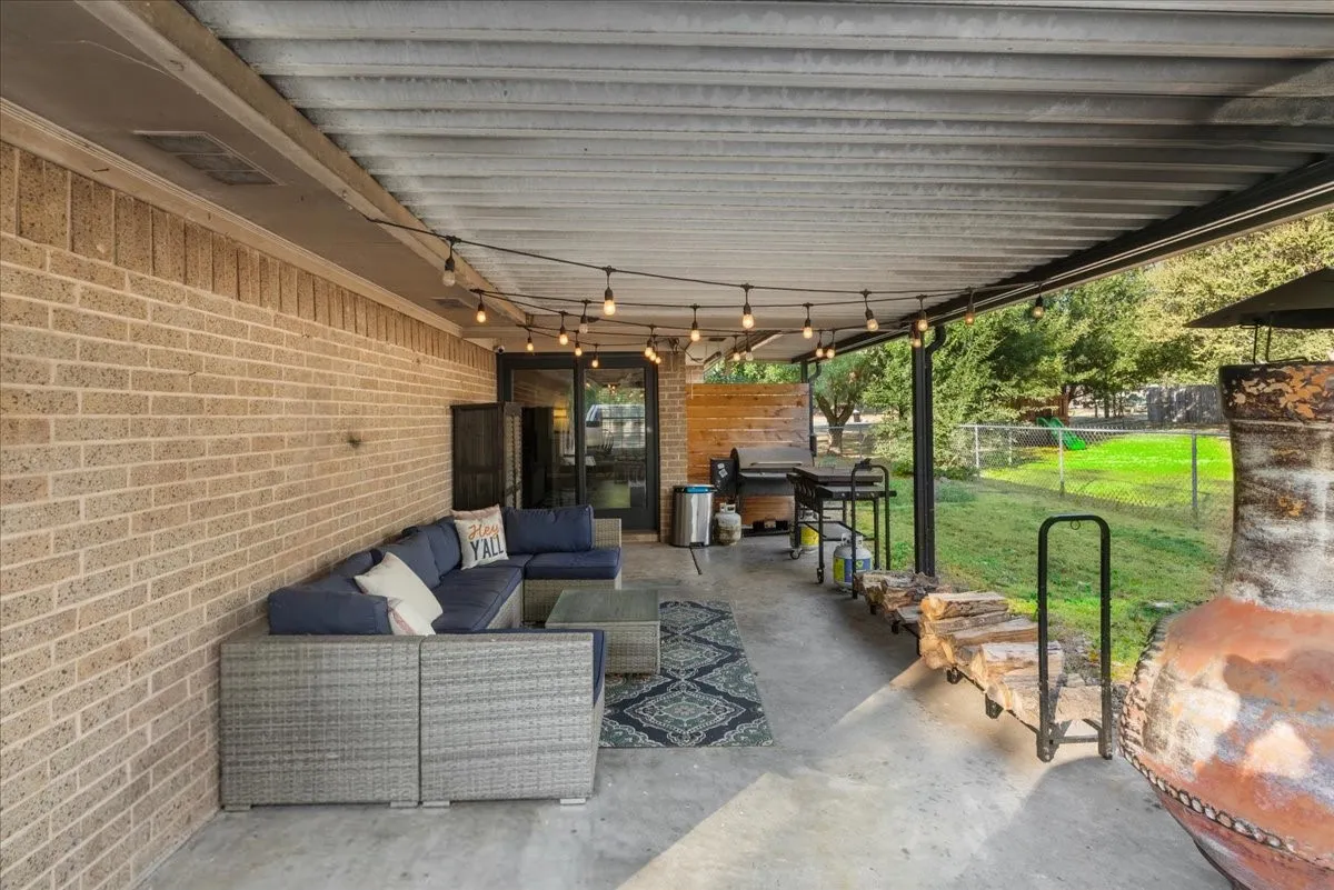 Covered patio with string lighting, concrete flooring, and a brick exterior wall