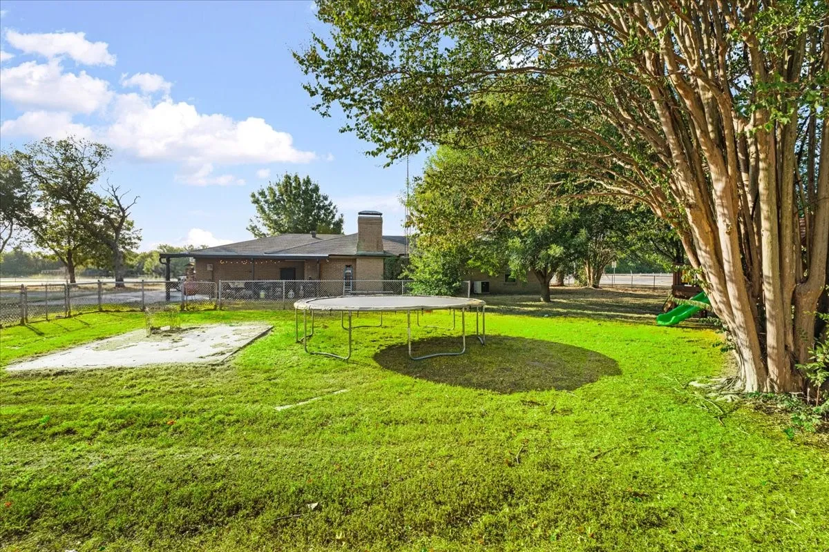 Expansive green lawn with mature trees and a chain-link fence