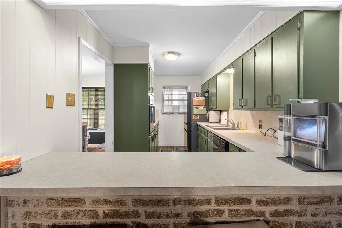 Kitchen with a pass-through bar featuring a brick-finish base, laminate countertop, dark green cabinetry, and white paneled walls