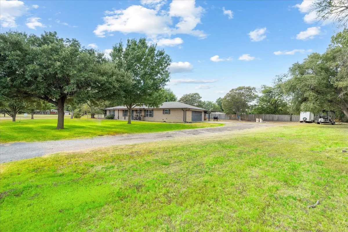 Expansive grassy grounds with mature trees and a gravel driveway leading to the residence