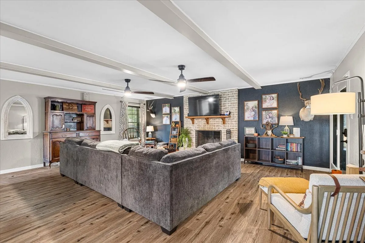 Living area featuring wood-finish flooring, exposed ceiling beams, and a brick-surround fireplace