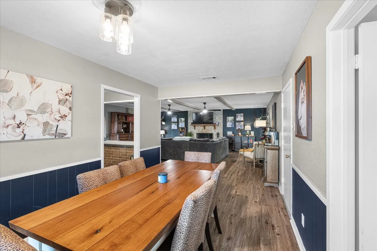 Wood-finish flooring throughout, featuring a dining area with wainscoting, an open doorway, and a ceiling-mounted light fixture